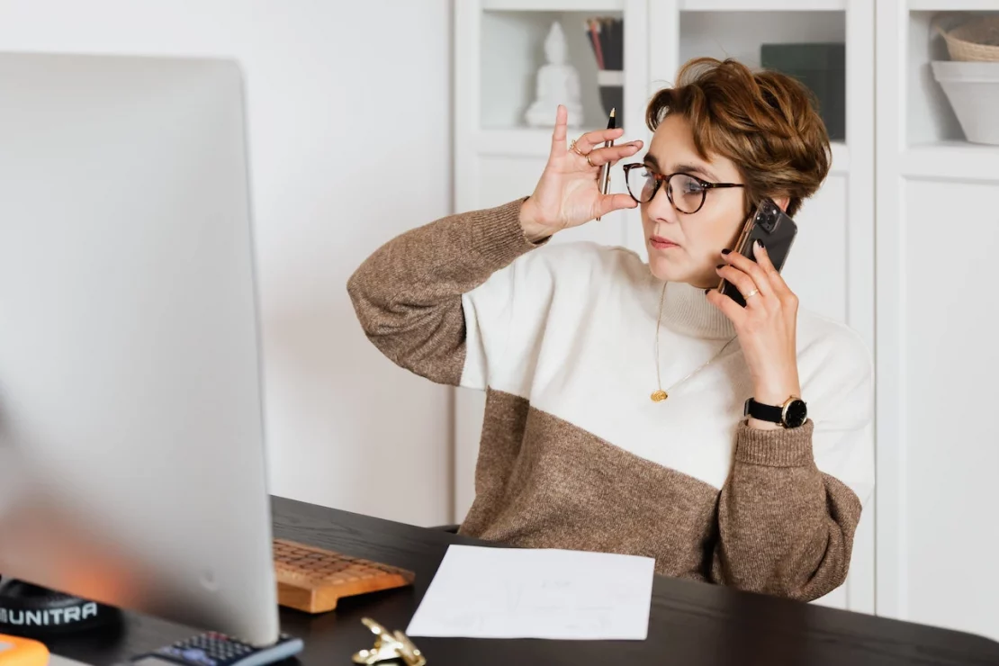 Frau sitzt am Schreibtisch und telefoniert mit einem Mobiltelefon